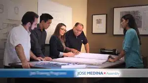 Five professionals gathered around a table examining architectural plans and blueprints.
