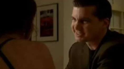 A man in a dark suit smiling while engaging in a conversation with a person out of frame.