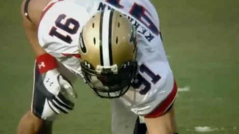 A football player wearing a white jersey with a gold helmet preparing for a play on the field.