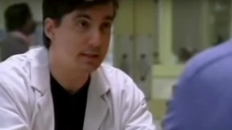 A doctor in a white coat engaged in conversation with a patient in a clinical setting.