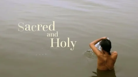 Individual bathing in a body of water with the words 'Sacred and Holy' overlaying the image.