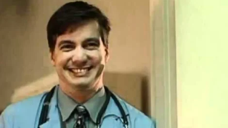 A male doctor wearing scrubs and a stethoscope smiling at the camera.