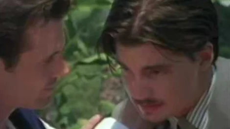 Two men with dark hair engaged in a serious conversation outdoors.