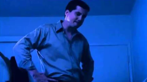 Man standing with hands on hips in a room illuminated by blue light.