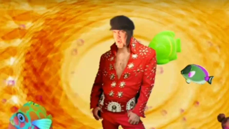 Man wearing a red Elvis-style costume with a black hat, posing against a colorful background.