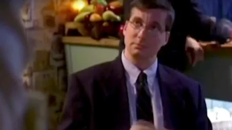 Man wearing a suit and glasses, looking attentively while standing indoors.