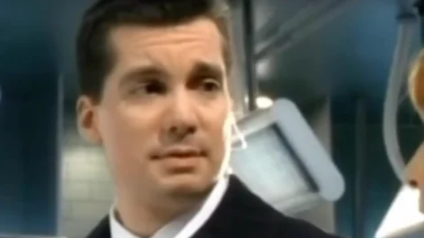 A man wearing a suit with a serious expression, looking slightly to the side in an indoor setting.