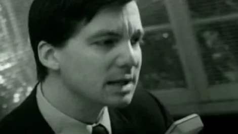 A man in a suit speaking intently, captured in black and white photography.
