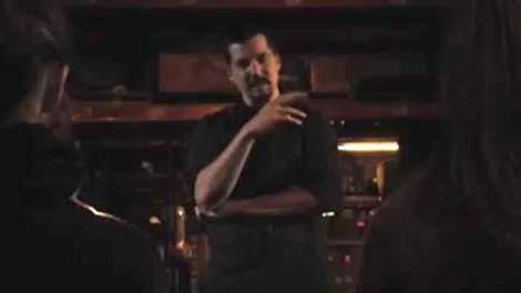A man gesturing while speaking to an audience in a dimly lit environment.